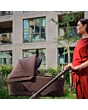 1518099110_F8_2026_maxicosi_stroller_oxfordcarrycot_oaktruffle_lifestyle_momcheckingcarrycotside